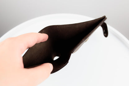 A hand holding a dark brown leather pouch or card holder against a clean white background.