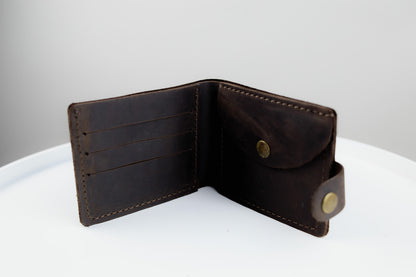 A dark brown leather bi-fold wallet shown open, displaying its interior card slots and pocket, set against a clean white and light gray background.