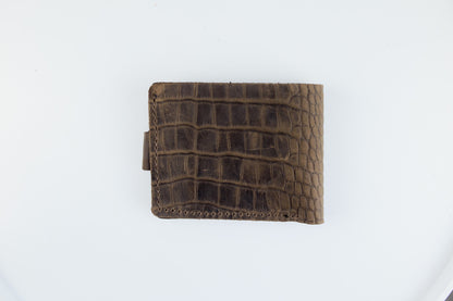 A brown leather bifold wallet with an alligator or crocodile-embossed texture, shown closed on a plain white background.