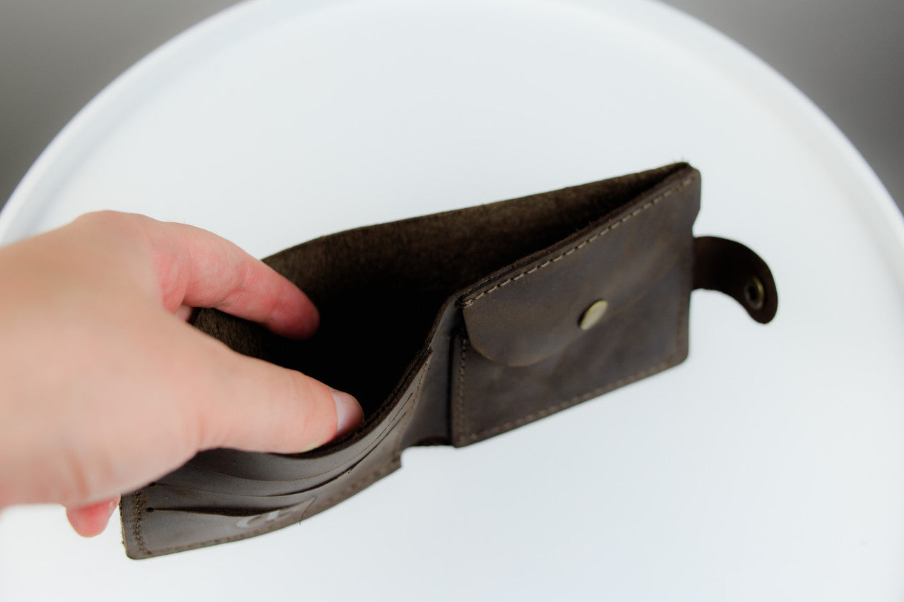 A dark brown leather wallet with multiple card slots and a small side loop, held open by a hand against a white circular background.