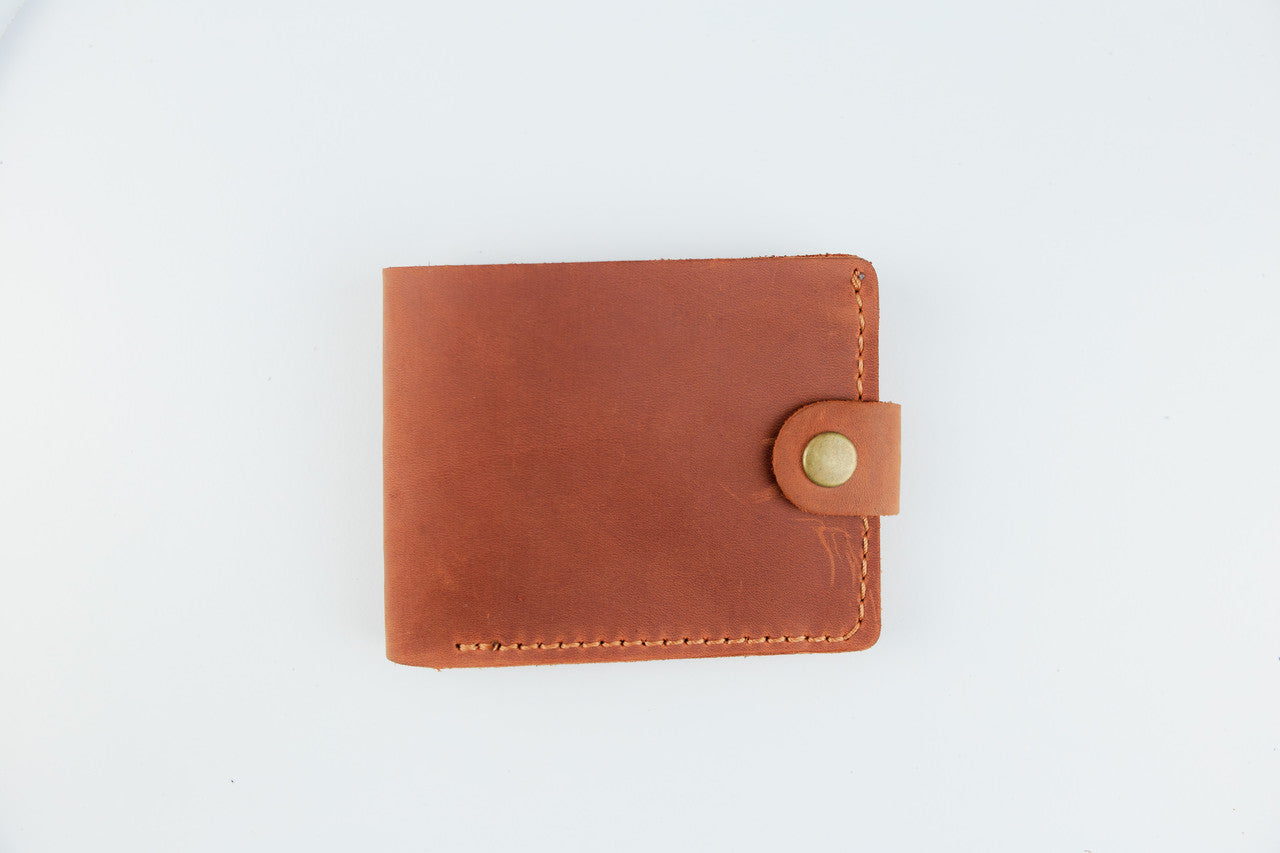 A brown leather bi-fold wallet with a snap-button closure, shown flat on a clean white background.