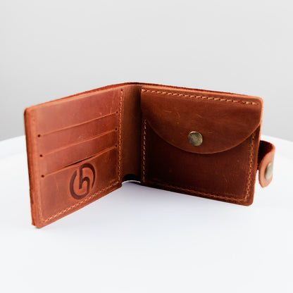 An open brown leather bifold wallet with card slots, a snap-button envelope pocket, and an embossed logo on the left panel, photographed on a white surface against a light gray background.