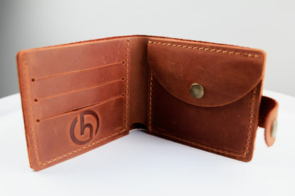 An open brown leather bifold wallet with card slots, a coin pocket, and a debossed logo on the left panel, photographed on a white surface against a light gray background.