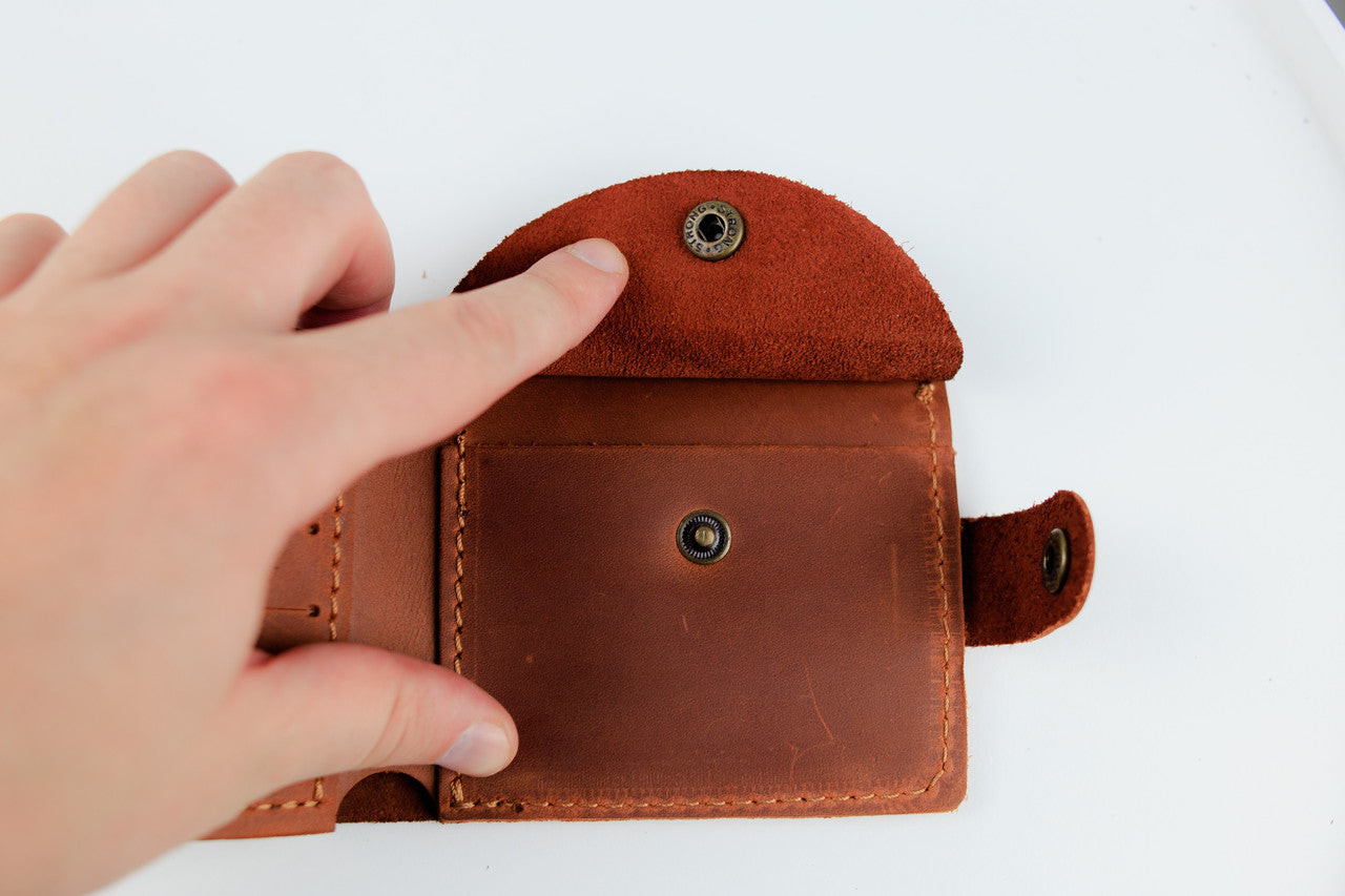 A close-up of a person's hand holding open a brown leather card holder wallet against a plain white background.