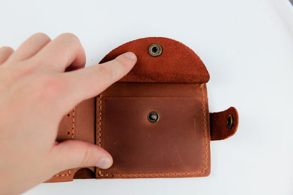 A close-up of a person's hand holding open a brown leather card holder wallet against a plain white background.