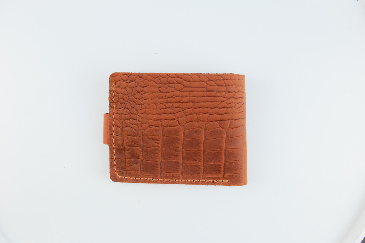 A brown leather bifold wallet with an embossed crocodile pattern and contrast stitching, shown on a plain white background.