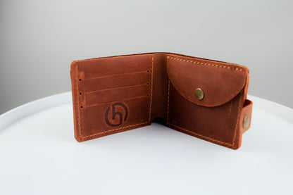 A brown leather bifold wallet shown open, revealing card slots on one side and a pocket flap with a snap button on the other. The interior has a debossed geometric logo, and the wallet is photographed on a white surface against a light gray background.