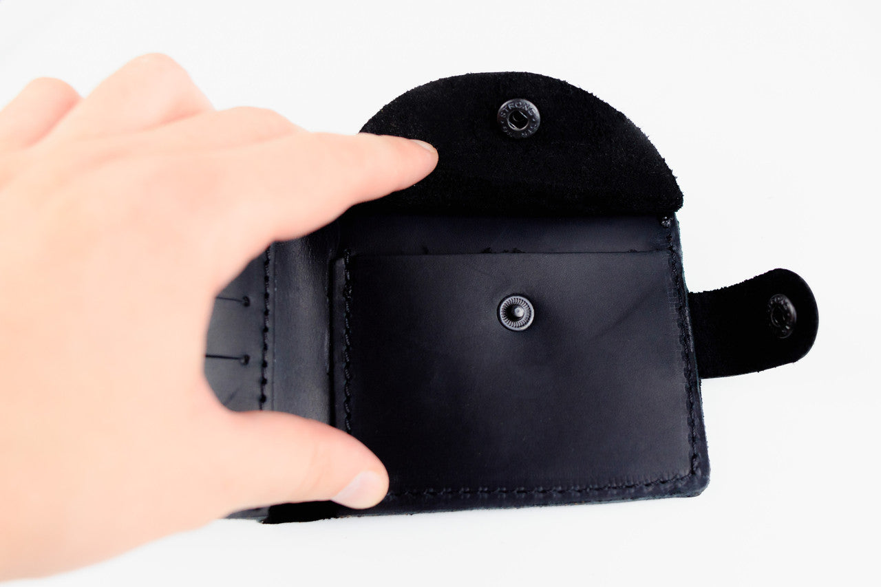 A black leather card holder wallet with a flap closure and snap button, held open by a hand against a plain white background.
