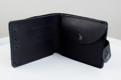 A black leather bifold wallet shown open, displaying its interior card slots, a snap-button pocket, and a small attached loop on a plain white surface.