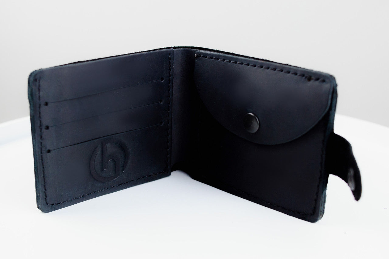 A black leather bifold wallet shown open, featuring card slots on the left, a pen slot with a snap button on the right, and a small hanging loop on the edge, photographed on a white surface.