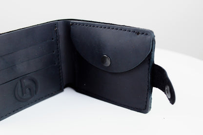 A black leather bifold wallet shown open, featuring card slots on the left, a card pocket with a snap closure on the right, and a small black strap with a snap button on the side.