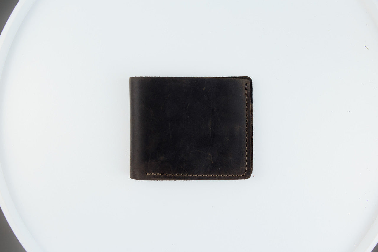 A dark brown leather bifold wallet with visible stitching, placed flat on a white circular surface.