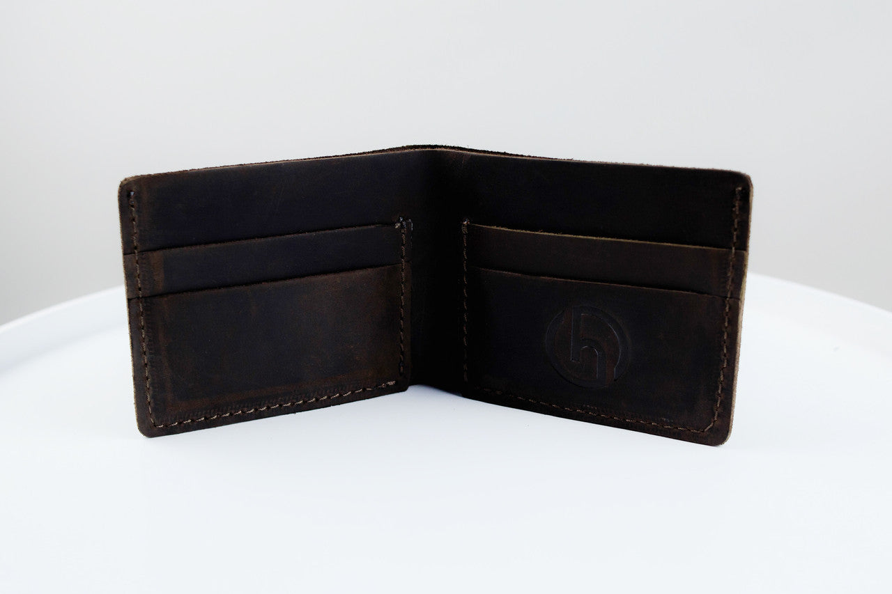 An open dark brown leather bifold wallet with card slots and an embossed logo on the inside right panel, photographed on a white surface against a light gray background.