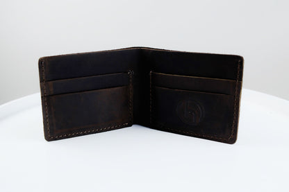 An open dark brown leather bifold wallet with card slots and an embossed logo on the inside right panel, photographed on a white surface against a light gray background.
