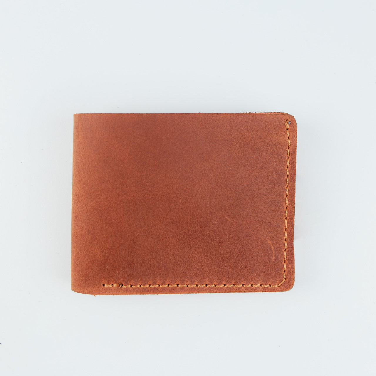 A minimalist brown leather bifold wallet with visible hand-stitched edges, photographed flat against a clean white background.