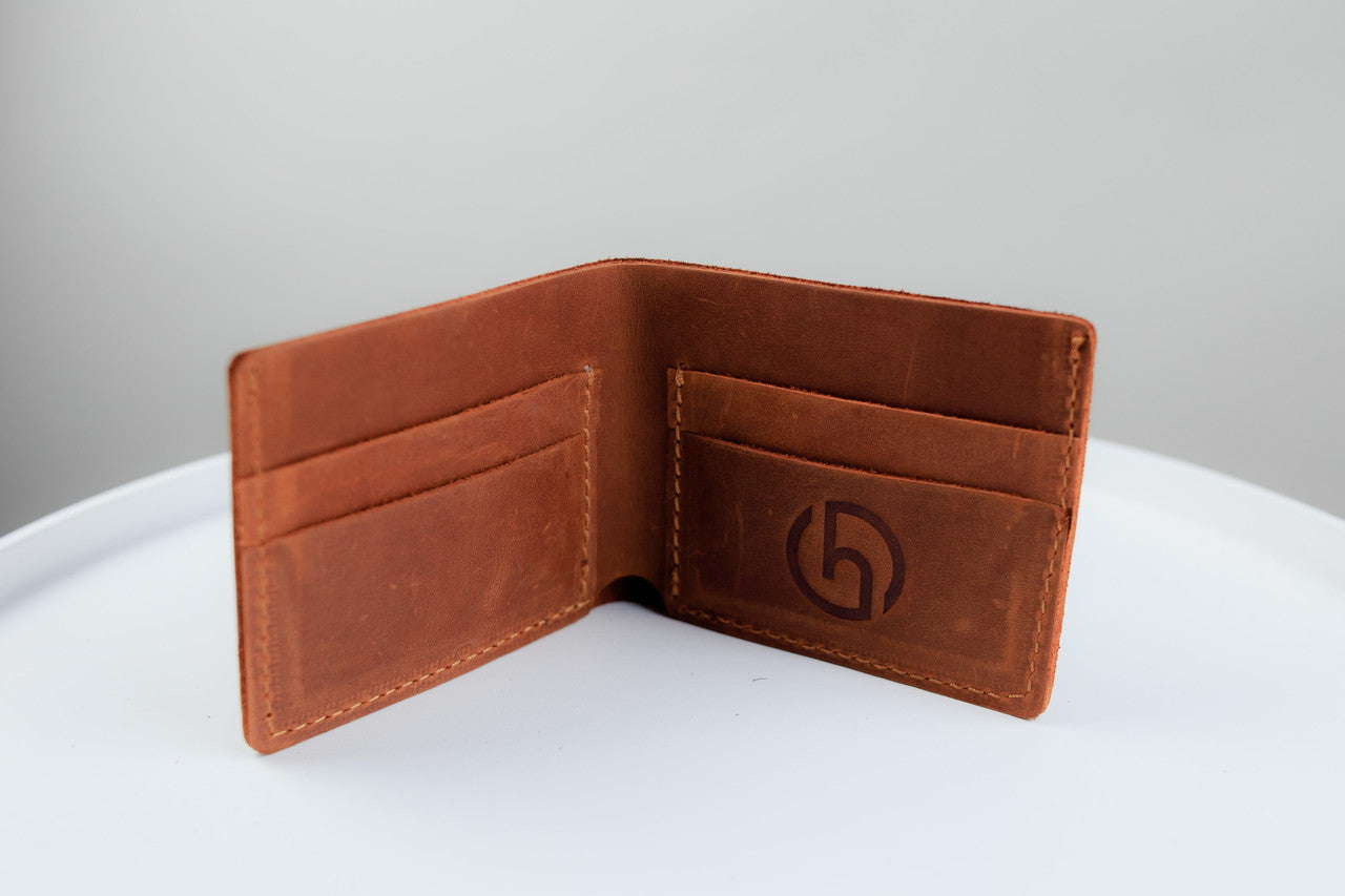 A brown leather bifold wallet shown open, displaying its interior card slots and a debossed circular logo on the right pocket, set against a neutral gray background on a white surface.