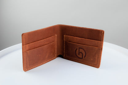 A brown leather bifold wallet shown open, displaying its interior card slots and a debossed circular logo on the right pocket, set against a neutral gray background on a white surface.