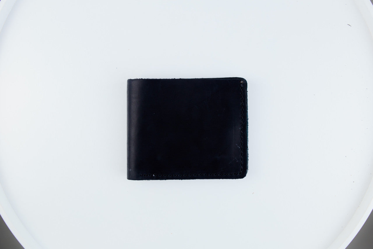 A black leather bifold wallet centered on a white circular surface.