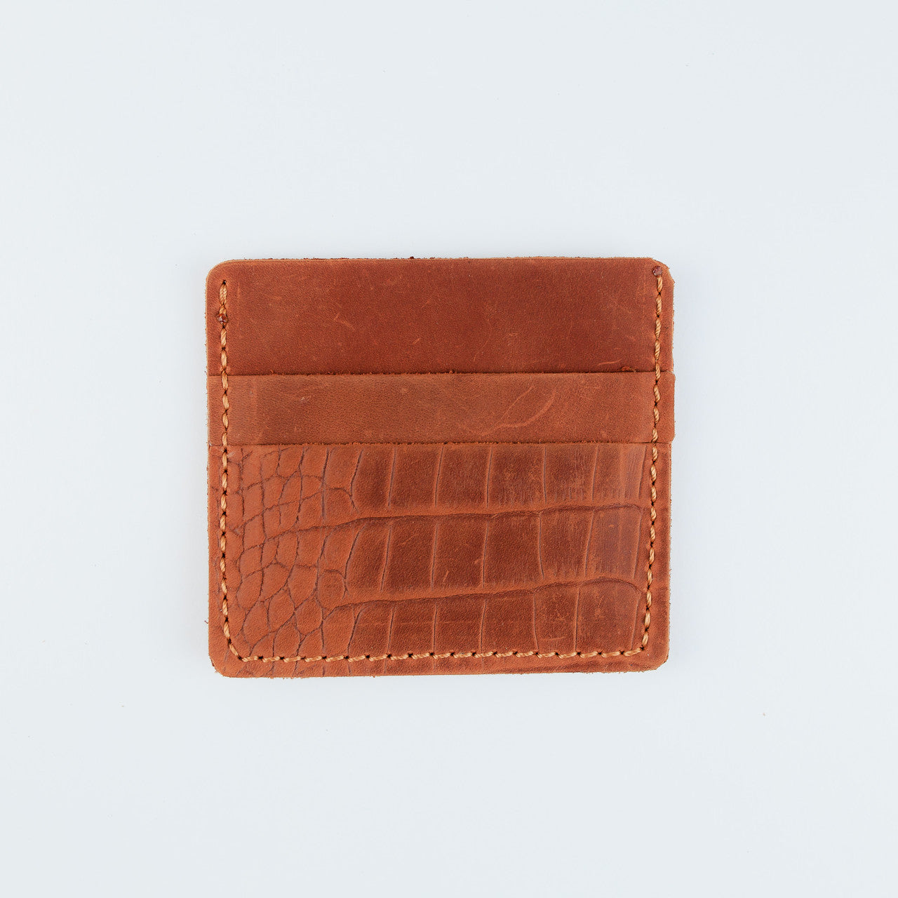 A small brown leather card holder or wallet with a crocodile-embossed texture on the front, shown flat against a light gray background.