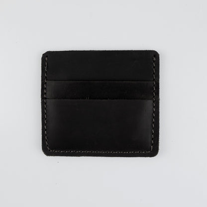 A minimalist black leather card holder with visible contrast stitching, photographed flat against a light gray background.