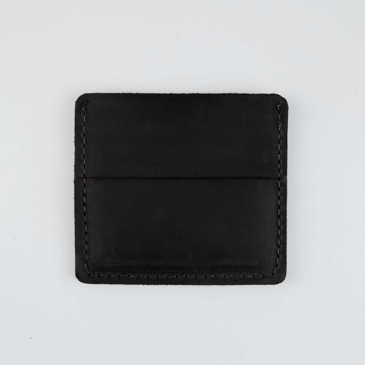 A minimalist black leather card holder or wallet with visible stitching, photographed flat against a light gray background.