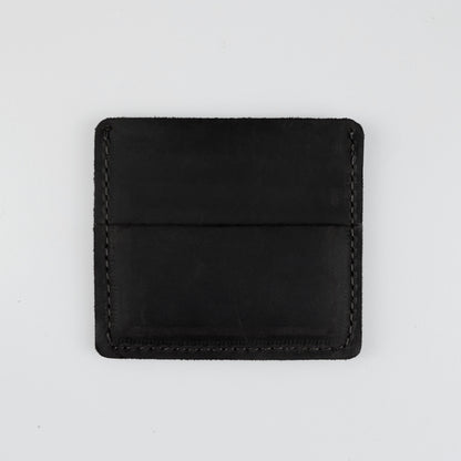 A minimalist black leather card holder or wallet with visible stitching, photographed flat against a light gray background.