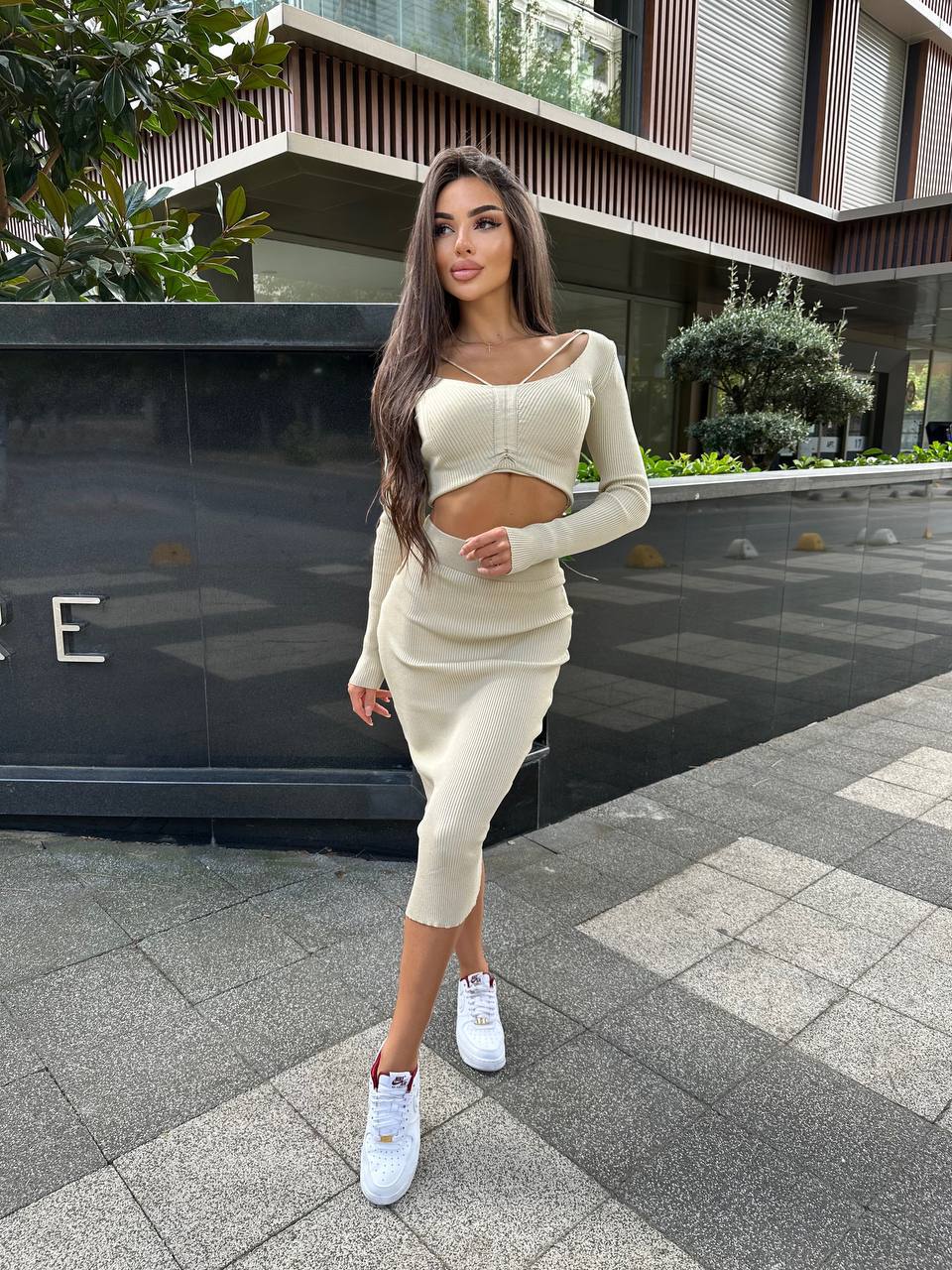 Woman in a beige outfit standing on a sidewalk with a building in the background