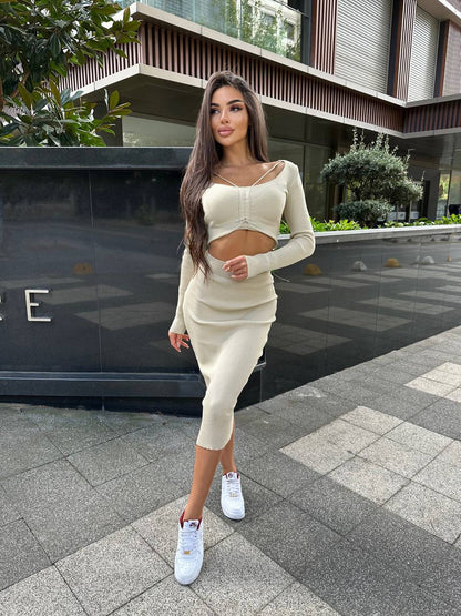 Woman in a beige outfit standing on a sidewalk with a building in the background