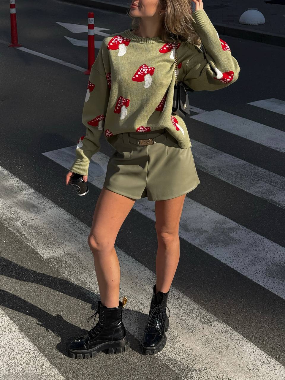 Person wearing a green sweater with red mushroom patterns and matching shorts on a street.