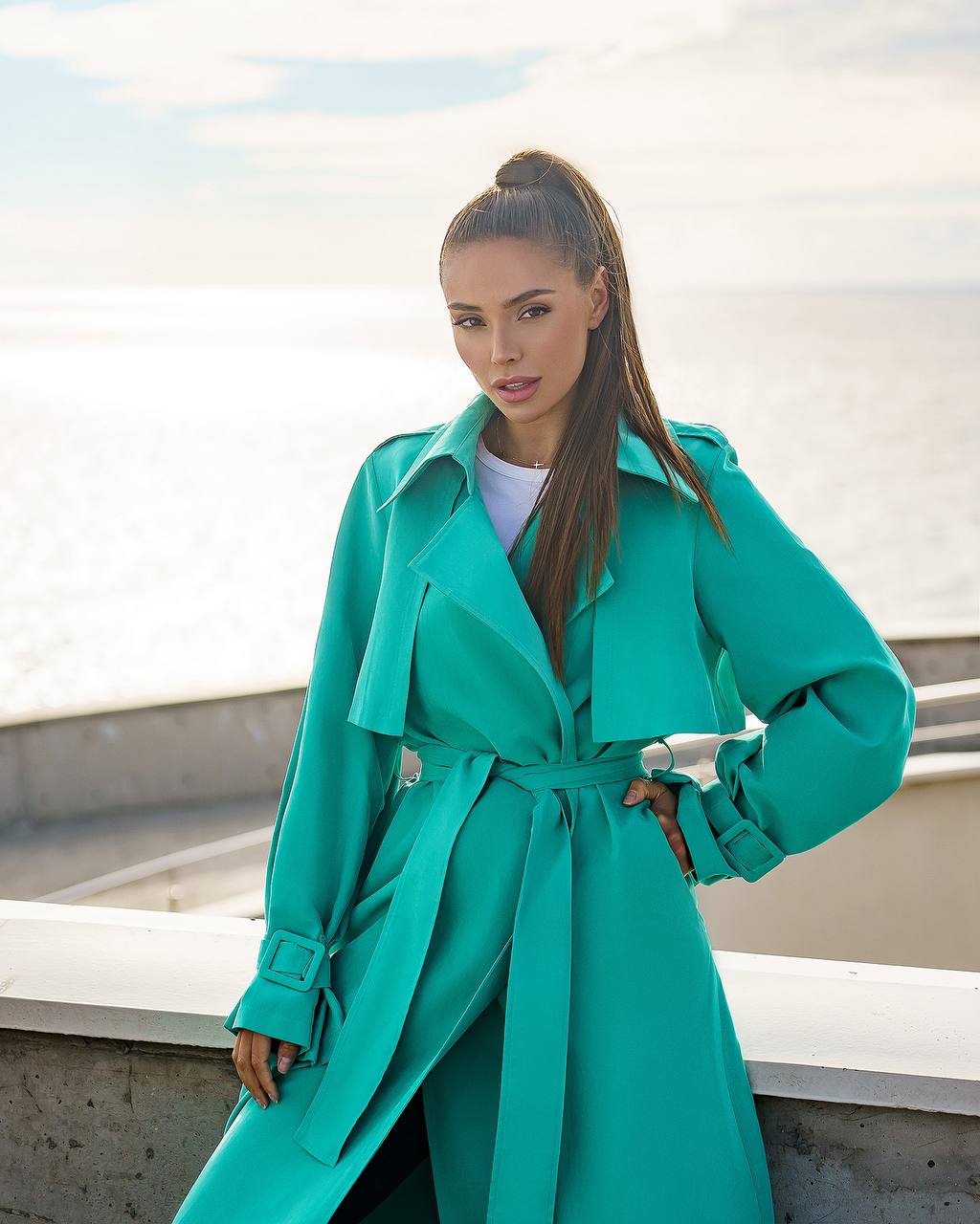 Woman wearing a teal coat standing outdoors with a light background