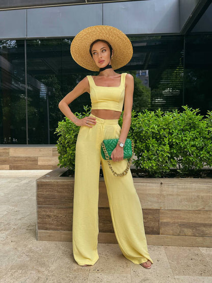 Woman in yellow outfit with wide-brimmed hat and green clutch standing outdoors.