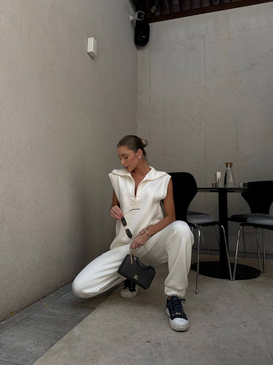 Woman in a white outfit sitting on the floor in a minimalistic room.
