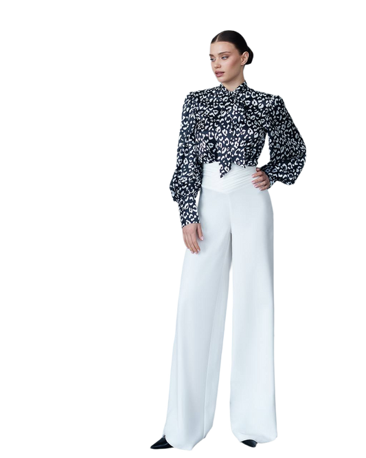 Woman wearing a black and white patterned blouse with white pants on a white background