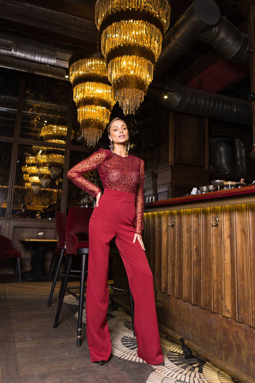 Woman in a red outfit standing in a stylish bar with chandeliers.
