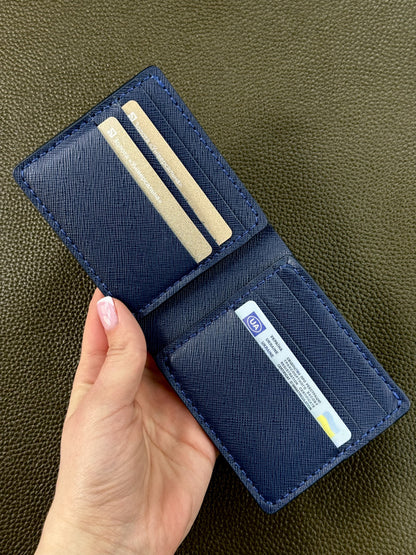 A navy blue textured leather bifold wallet held open by a hand, showing its interior card slots and ID pocket against a dark olive green textured background.