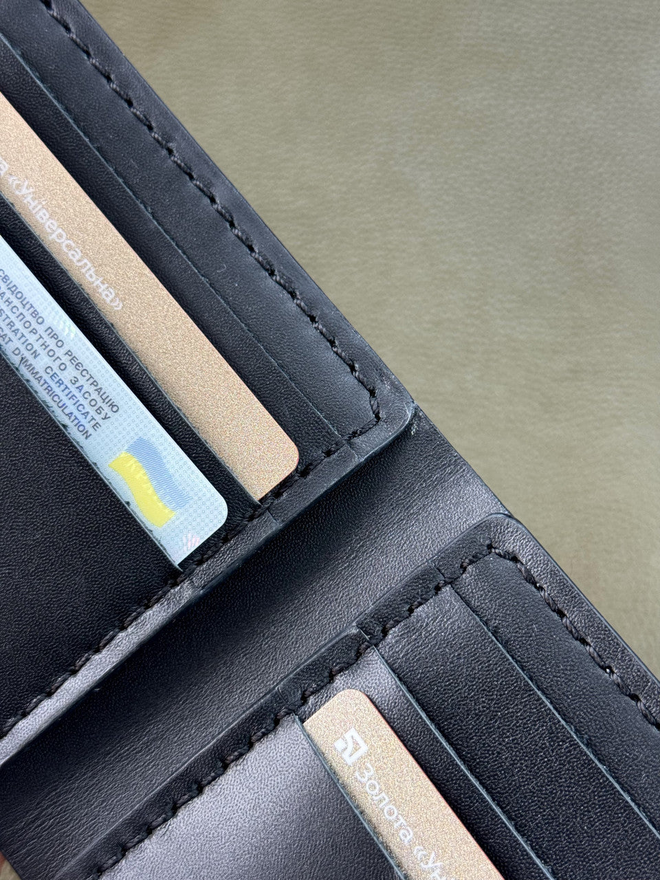 Close-up of a black leather wallet showing card slots with credit cards inserted, on a neutral gray background.