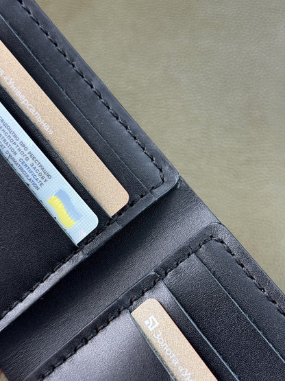 Close-up of a black leather wallet showing card slots with credit cards inserted, on a neutral gray background.
