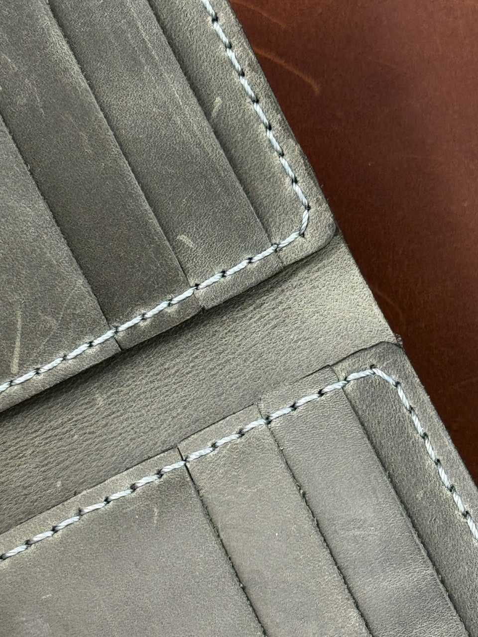 Close-up of a gray leather wallet showing stitched card slots and interior lining, with a brown surface visible at the upper right.