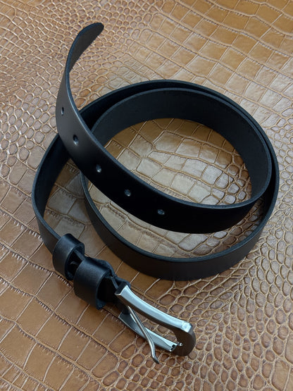 A black leather belt with a silver-toned metal buckle, coiled on a textured tan crocodile-embossed surface.