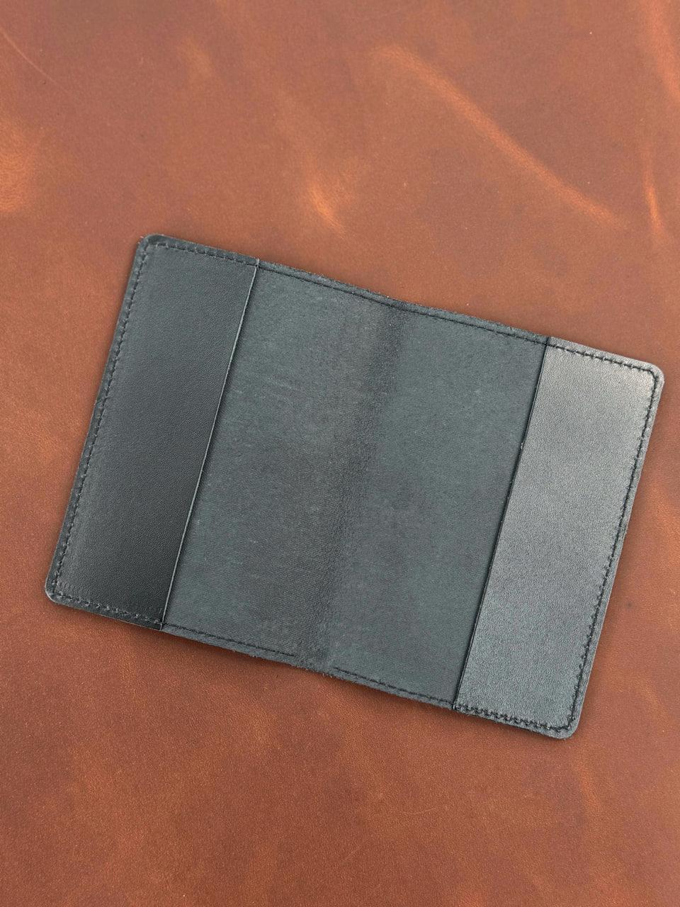 A dark gray leather card holder wallet shown open on a textured brown leather background.