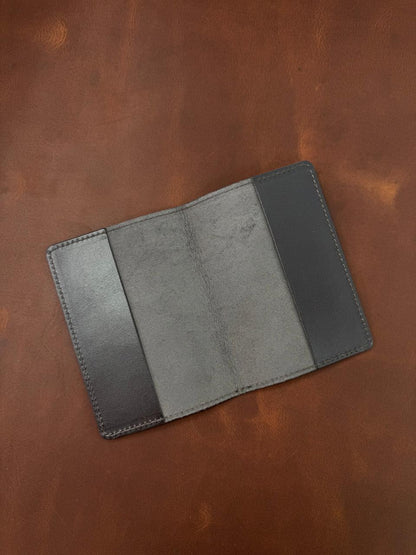 A dark gray leather bifold wallet shown open, displaying its interior card slots and stitched edges, placed on a textured brown leather background.