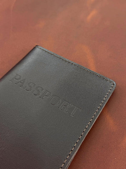 A close-up of a dark brown leather passport cover with 'PASSPORT' embossed on the front, resting on a textured brown leather surface.