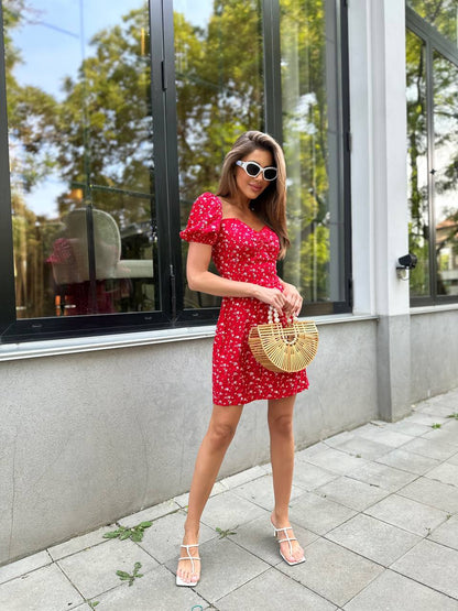Woman in a red dress with white polka dots standing outside a building.