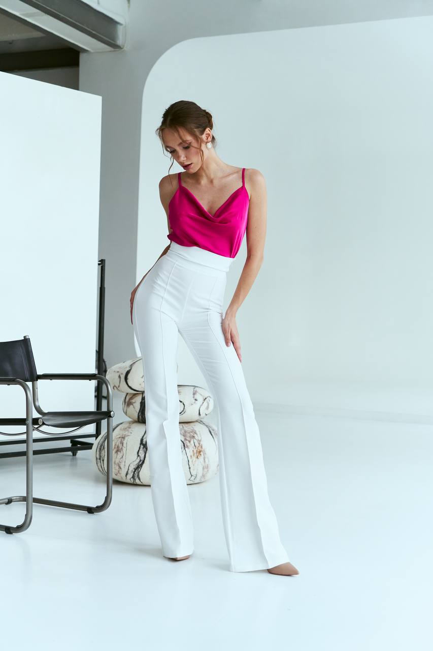 Woman wearing a pink top and white pants in a minimalistic room.