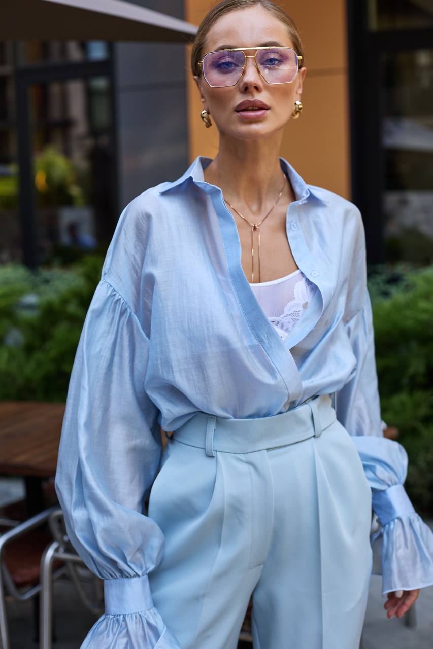Woman wearing a light blue outfit with sheer sleeves in an outdoor setting