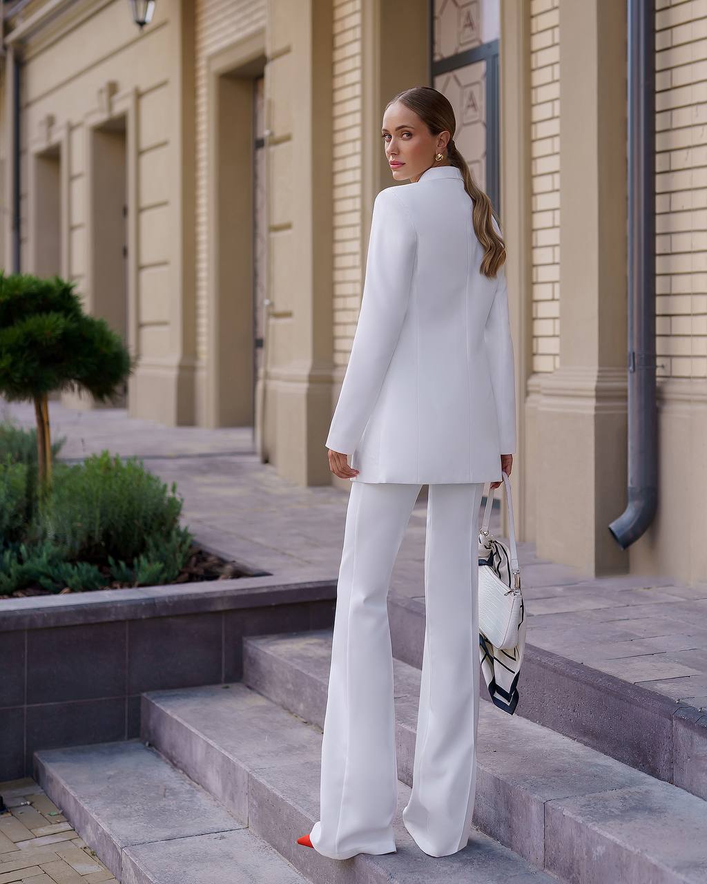 Woman in a white outfit standing on steps outside a building