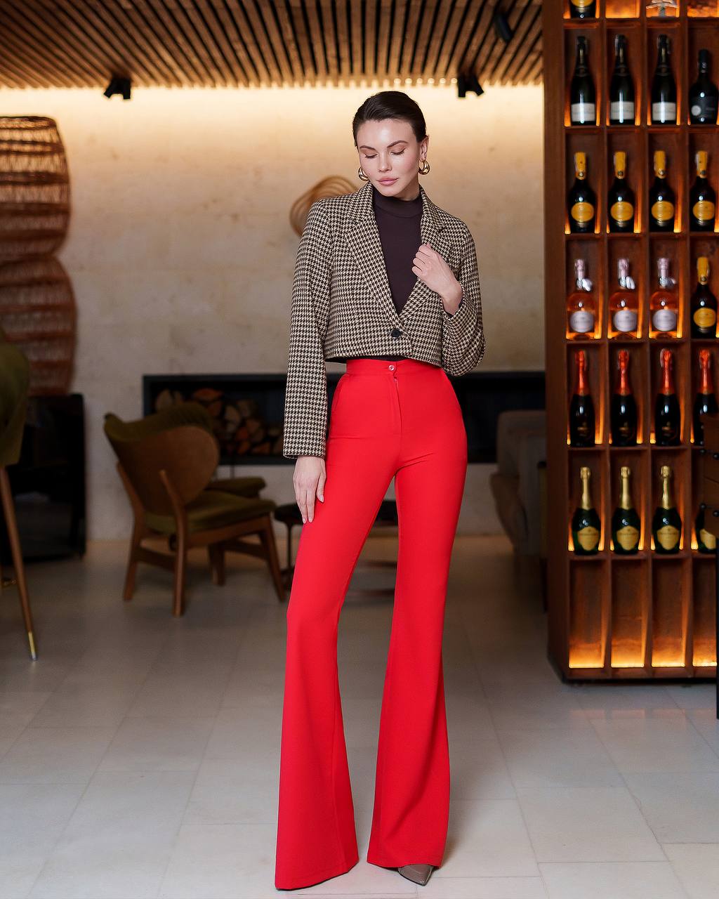 Woman wearing a patterned blazer and red pants in a stylish interior setting.