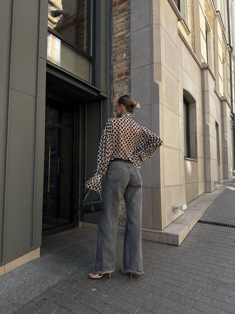 Person walking on a city street wearing a patterned blouse and high-waisted jeans.
