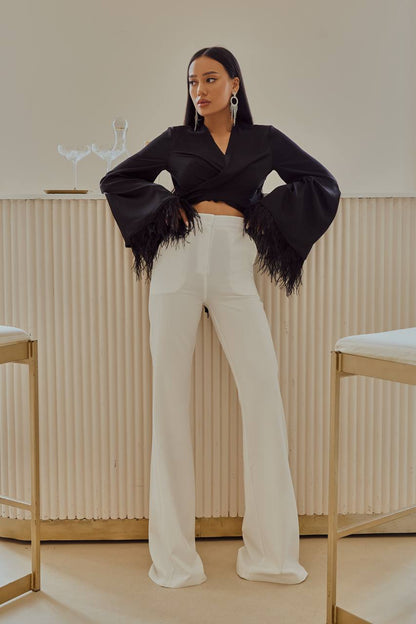 Woman wearing a black fringed jacket and white pants in a minimalistic setting
