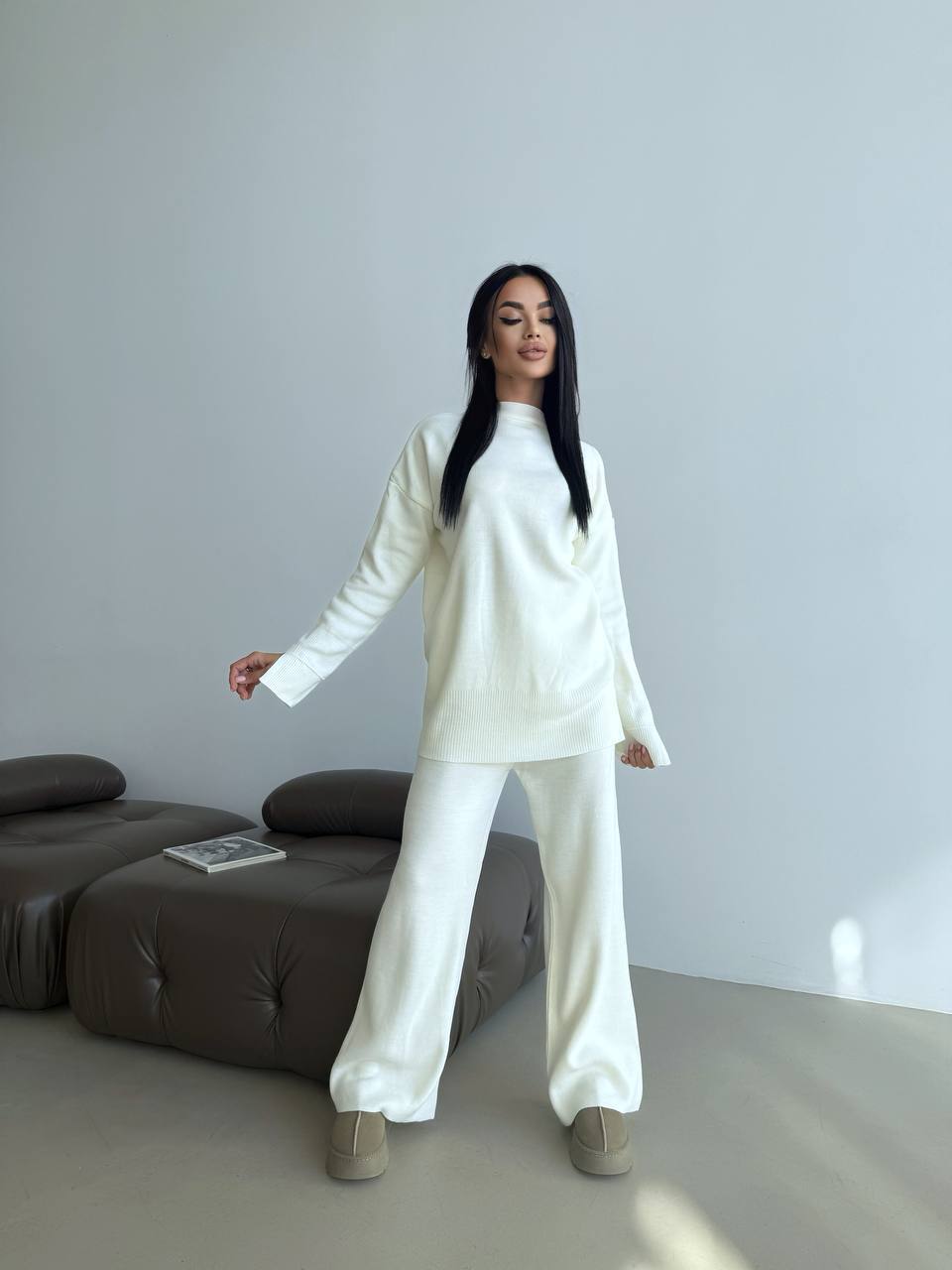 Person wearing a white outfit standing in a minimalistic room with a gray sofa.